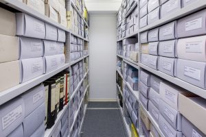 Blick zwischen Regale, Archivboxen und Ordner