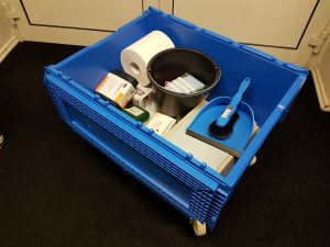 Zu sehen ist eine geöffnete blaue Notfallbox. Sie beinhaltet beispielsweise Kehrblech und Besen, eine Papierrolle, einen Eimer, Frischhaltefolie und Werkzeug.