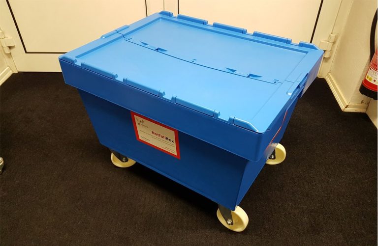 Man sieht eine geschlossene blaue Notfallbox aus Hartplastik mit Räollenn