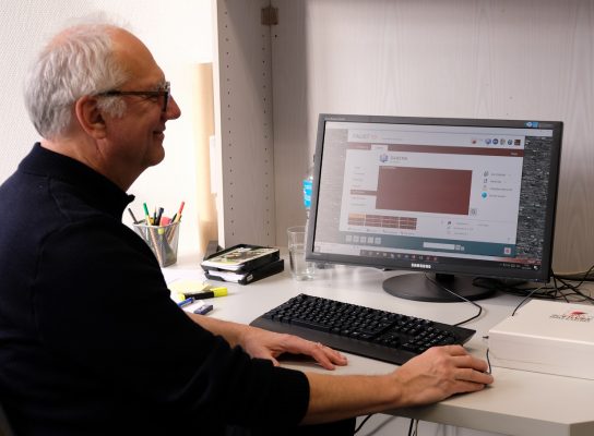 Christoph Fuchs sitzt am Schreibtisch, auf dem Computer-Monitor ist der FAUST-Startbildschirm zu erkennen.