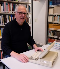 Christoph Fuchs am geöffneten Toshiba 1200 (Bildschirm hochgeklappt, im Hintergrund Bibliotheksregale